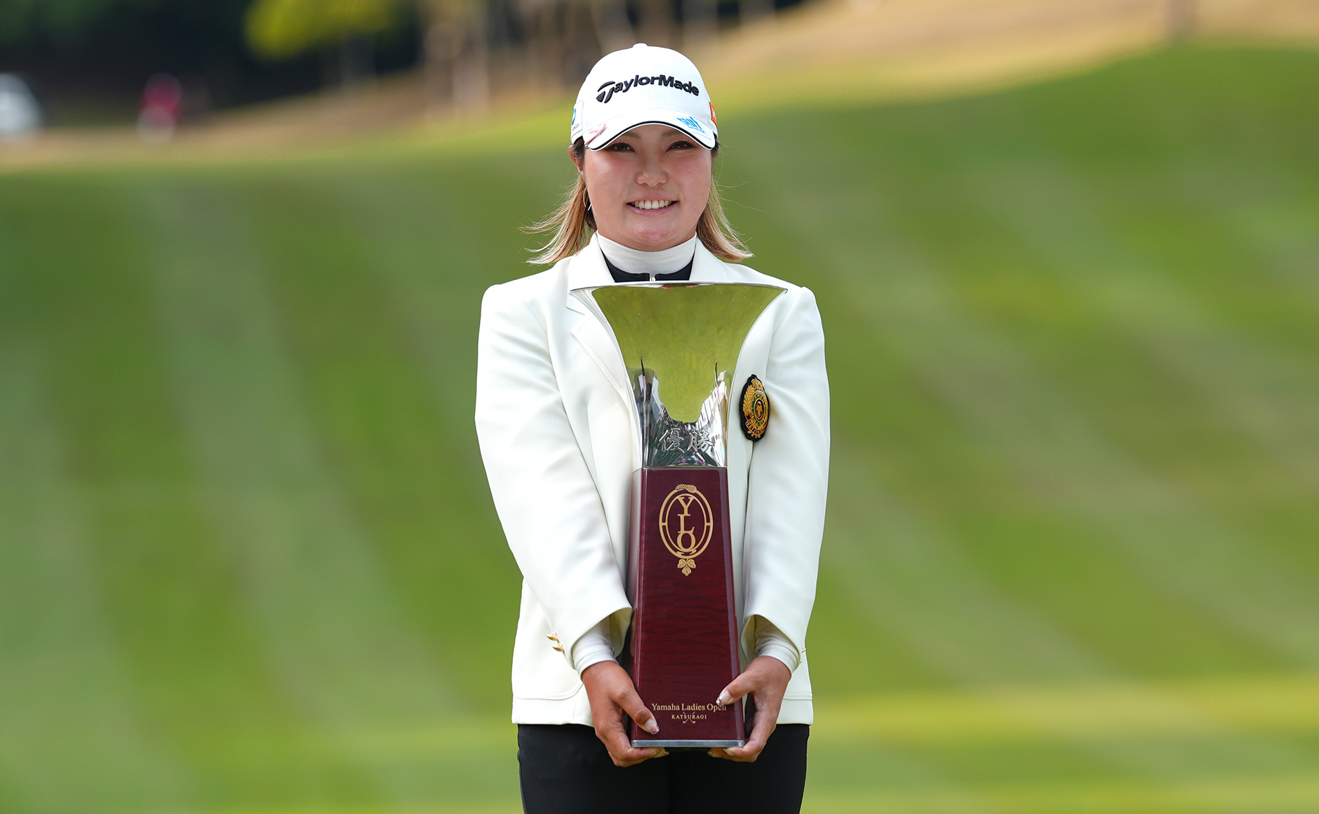 代々引き継がれている優勝者の白いジャケットを着用し、優勝トロフィーを体の前に抱える高橋彩華